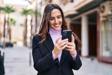 Young hispanic woman smiling confident using smartphone at street