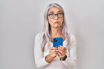 Middle age woman with grey hair using smartphone typing message depressed and worry for distress, crying angry and afraid. sad expression.