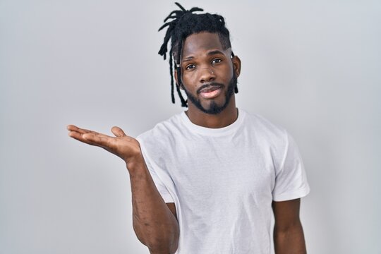 African man with dreadlocks wearing casual t shirt over white background smiling cheerful presenting and pointing with palm of hand looking at the camera.