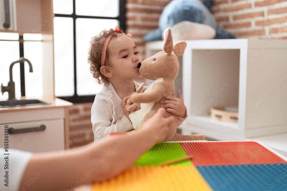 Poster adorable caucasian girl kissing kangaroo toy standing at kindergarten