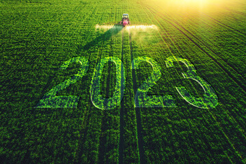 2023 Happy New Year agricultural business concept. Aerial view of farming tractor plowing and spraying on green field.