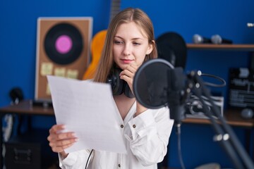 Young caucasian woman artist reading song with doubt expression at music studio