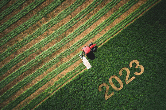 2023 Happy New Year concept and red tractor mowing green field