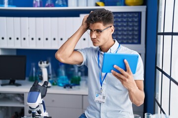 Naklejka na ściany i meble Young hispanic man scientist using touchpad with doubt expression at laboratory