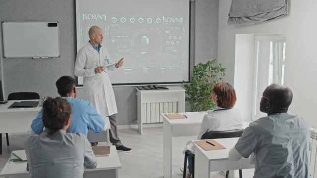 Modern mature Caucasian doctor holding digital tablet making presentation of new medical technology or treatment method