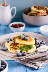 Pancakes with blueberries, sour cream and mint on a plate on the table. Homemade baking. Vertical