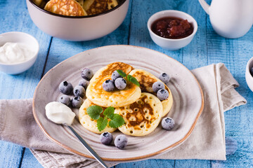 A plate of pancakes with blueberries, sour cream and mint on the table. Homemade pastry.