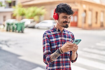 Young hispanic man smiling confident listening to music at street