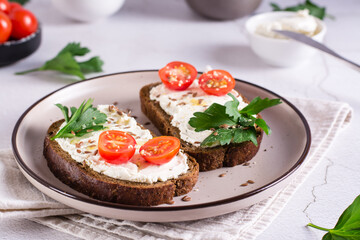 Appetizing bruschetta with ricotta, tomatoes, flax seeds and parsley on a plate on the table.