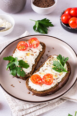 Sandwiches on rye bread with ricotta, tomatoes and parsley on a plate on the table. Vertical view