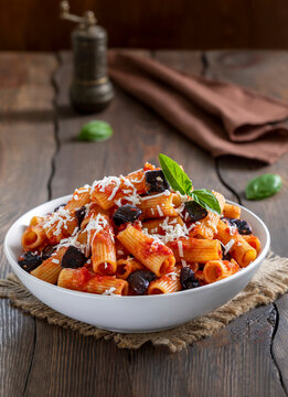 Pasta Alla Norma. Delicious Sicilian pasta dish with roasted eggplant, marinara tomato sauce, grated ricotta and fresh basil served in a white ceramic bowl. Wooden table, selective focus, vertical.