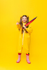 A child in a raincoat and scarf, in rubber red boots on a yellow isolated background. Rainy spring autumn weather. Clothes for the rain.