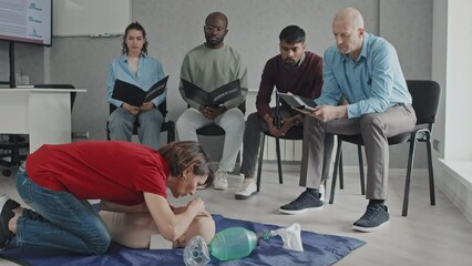 Mature woman sitting on floor using dummy to demonstrate CPR process at medical training course