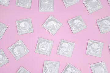 Many white packages of unopened condoms on a pink background.