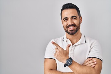 Young hispanic man with beard wearing casual clothes over white background with a big smile on face, pointing with hand finger to the side looking at the camera.