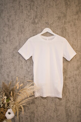 White shirt blank mockup on a hanger on the grey background with dry grass

