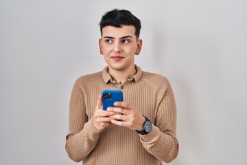 Non binary person using smartphone typing message smiling looking to the side and staring away thinking.