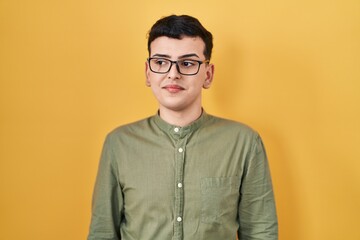 Non binary person standing over yellow background smiling looking to the side and staring away thinking.