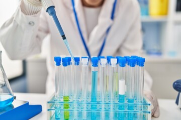 Young hispanic woman wearing scientist uniform using pipette at laboratory