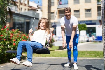 Obraz na płótnie Canvas Father and daughter smiling confident playing on swing at playground