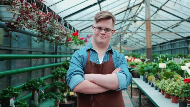 Happy male florist with down syndrome looking at the camera in the greenhouse