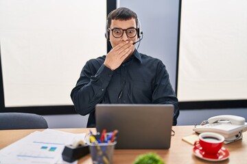 Young arab man wearing call center agent headset covering mouth with hand, shocked and afraid for...