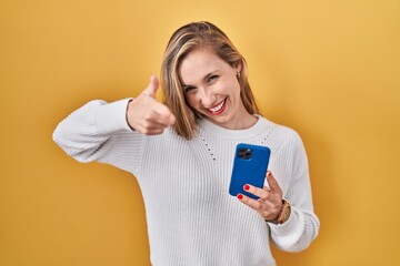 Naklejka premium Young blonde woman using smartphone typing message pointing fingers to camera with happy and funny face. good energy and vibes.