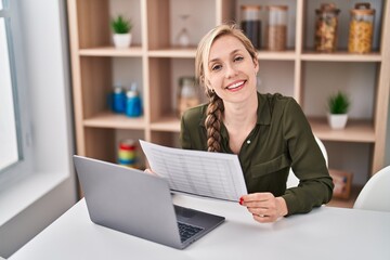 Young blonde woman using laptop reading document at home