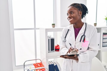 African american woman wearing doctor uniform writing on clipboard at clinic