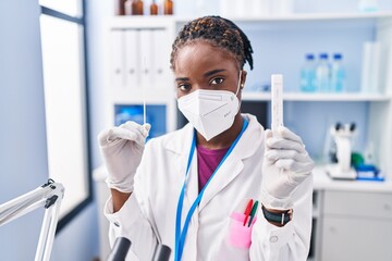 African american woman wearing scientist uniform and medical mask holding an at laboratory