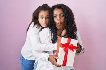 Mother and young daughter holding with presents making fish face with mouth and squinting eyes, crazy and comical.