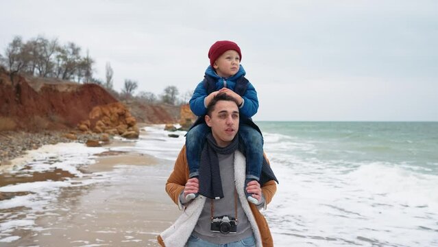 Concentrated father talking with his son on his neck on the beach near the sea