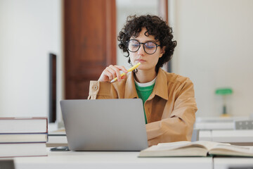 young woman in a library or coworking works laptop online, education and work creative project, diploma. female student reads book and conducts scientific work. Spanish confident business person