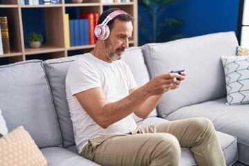 Obraz premium Middle age man playing video game sitting on sofa at home