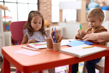 Fototapeta premium Adorable girl and boy sitting on table cutting paper at kindergarten