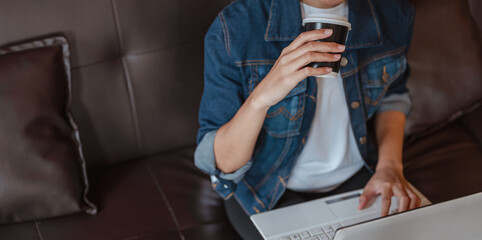 Close up top view of Asian woman student using laptop doing work at coffee shop.Business,Work and business woman concepts.she wear denims shirt.Business,Work and business woman concepts.
