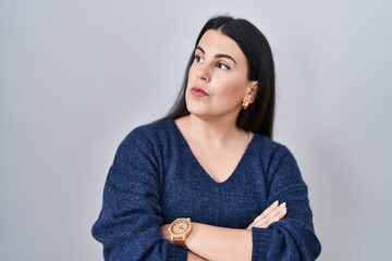 Young brunette woman standing over isolated background looking to the side with arms crossed convinced and confident