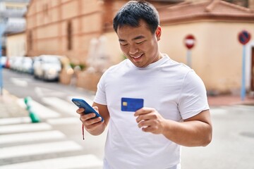 Young chinese man using smartphone and credit card at street