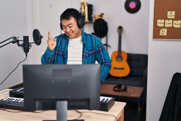Young chinese man looking at online music tutorial smiling happy pointing with hand and finger to...