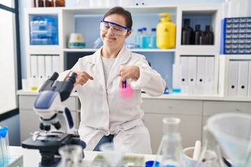 Hispanic girl with down syndrome working at scientist laboratory looking confident with smile on face, pointing oneself with fingers proud and happy.