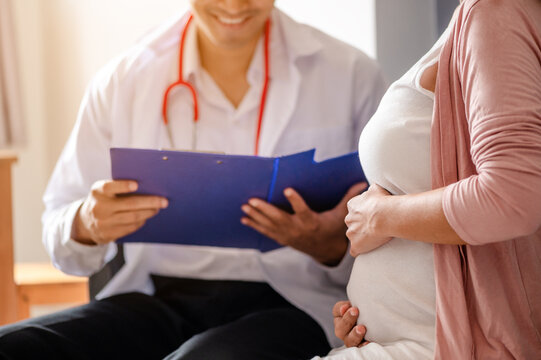 Close Up Of Male Doctor Hold Patient Have Consultation With Pregnant Woman In Hospital. Female Gynecologist Talk Consult Female Check Pregnancy Before Giving Birth. Maternity Concept.