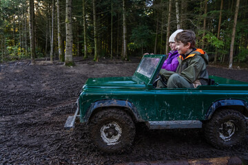 Children ride in an open iron children's car. Extreme form of entertainment for children. The boy drives through the mud, accompanied by his sister. High quality photo