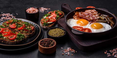 Tasty breakfast consists of eggs, bacon, beans, tomatoes, with spices and herbs © chernikovatv
