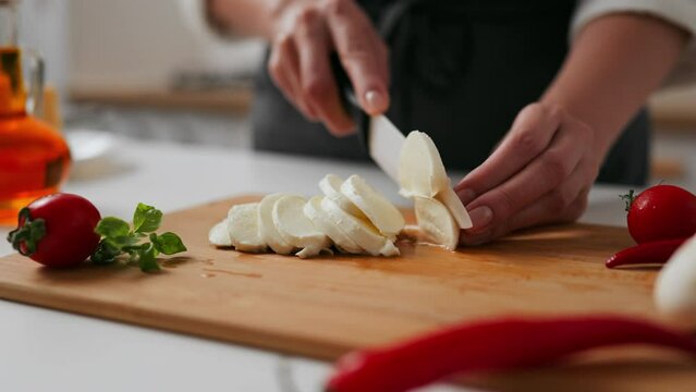 Chef cuts mozzarella cheese for cooking food for restaurant customers, cooked food process of cutting mozzarella cheese for pizza topping food preparation for baking pizza
