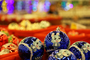 Christmas toys, blue balls with bunny - symbol of Chinese New Year 2023 on blurred festive lights background. New Year decorations in a store