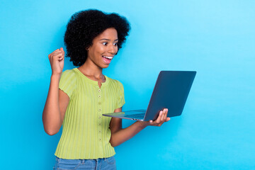 Obraz na płótnie Canvas Portrait of ecstatic overjoyed girl with wavy hairdo dressed green t-shirt look at laptop clench fist up isolated on blue color background