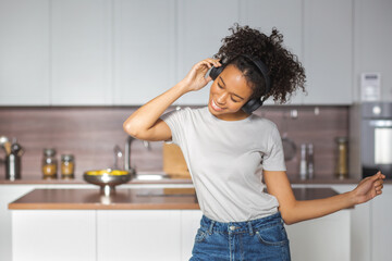 Happy woman with headphones dancing and listening music in the morning in her kitchen, relax at home