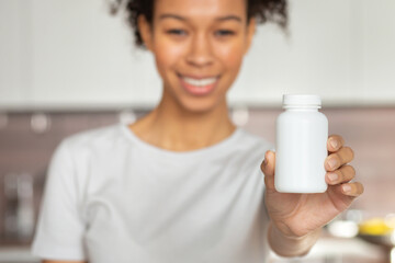 Happy young African American woman holding bottle of dietary supplements or vitamins in her hands. Close up. Healthy lifestyle concept