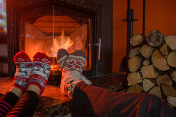 Feets in woollen socks by the Christmas fireplace. Couple sitting neat the fireplace, relaxes by...