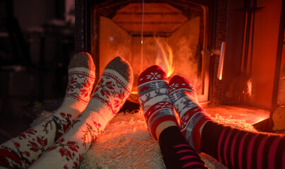 Feets in woollen socks by the Christmas fireplace. Couple sitting neat the fireplace, relaxes by warm fire and warming up their feet in woollen socks.